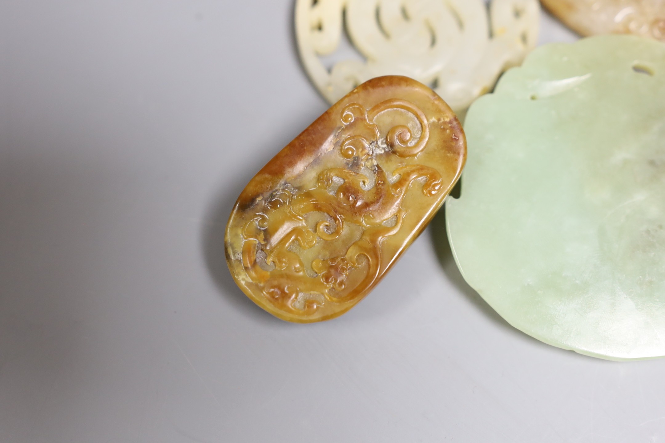 Four Chinese jade carvings, to include a face plaque, a dragon plaque, disc and a pebble carving, largest 6.5cm long, (4)